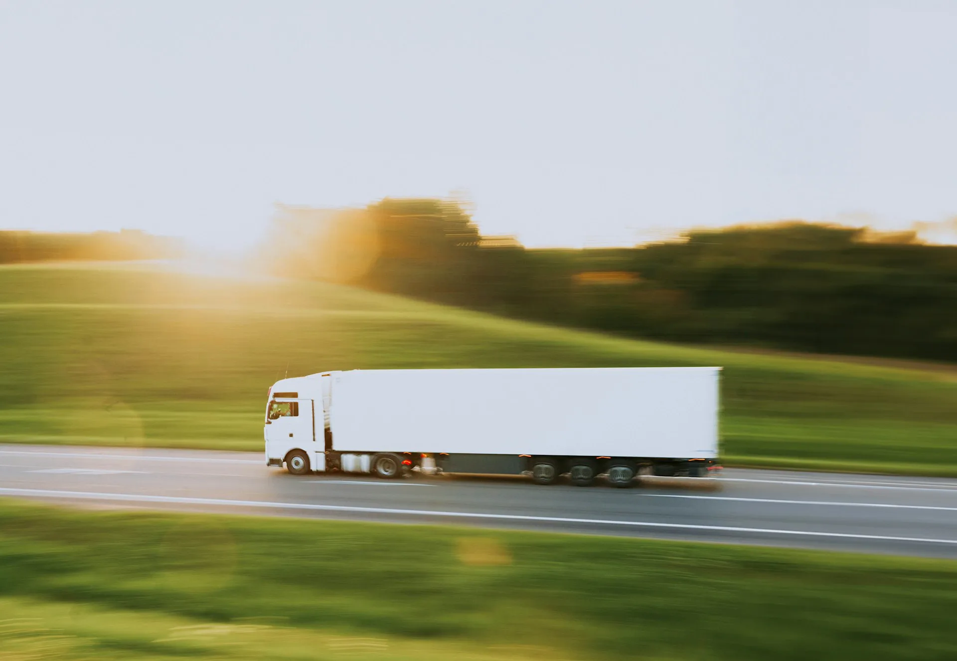 Long-haul truck and trailer in full side profile, in motion on a country road at golden hour — Torqen commercial friction systems built for heavy vehicles